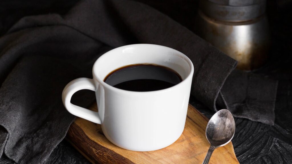 Secangkir kopi hitam dengan alas tatakan kayu (Freepik/Tokokopih.com)